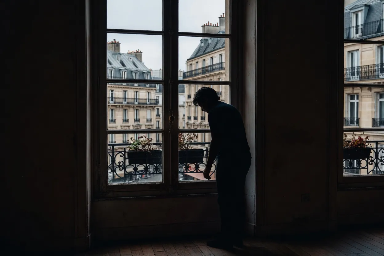 Silhouette pensive devant une fenêtre parisienne, ambiance de réflexion et d’introspection
