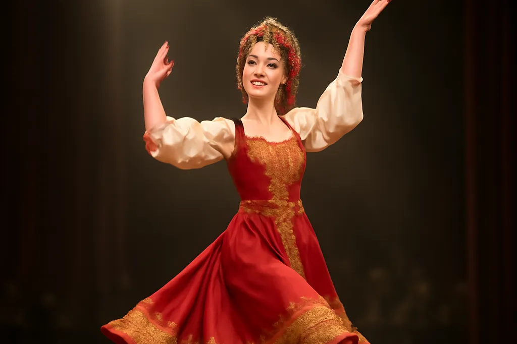 Danseuse en costume folklorique russe rouge et or exécutant une plyaska sur une scène parisienne